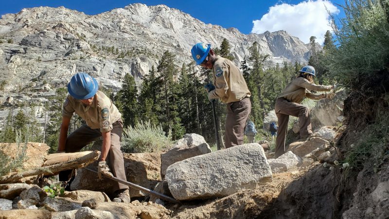 Backcountry Corpsmembers use hand tools to build new trail out of rock.