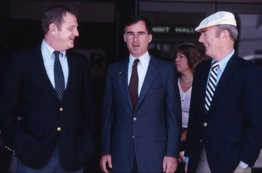 XJerryBrownBTDugan1982lifem Three men in suits stand around talking in the 1970s.