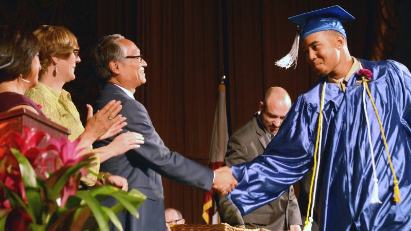 Image of Corpsmember in cap and gown shaking hands with CCC Director Bruce Saito during graduation ceremony