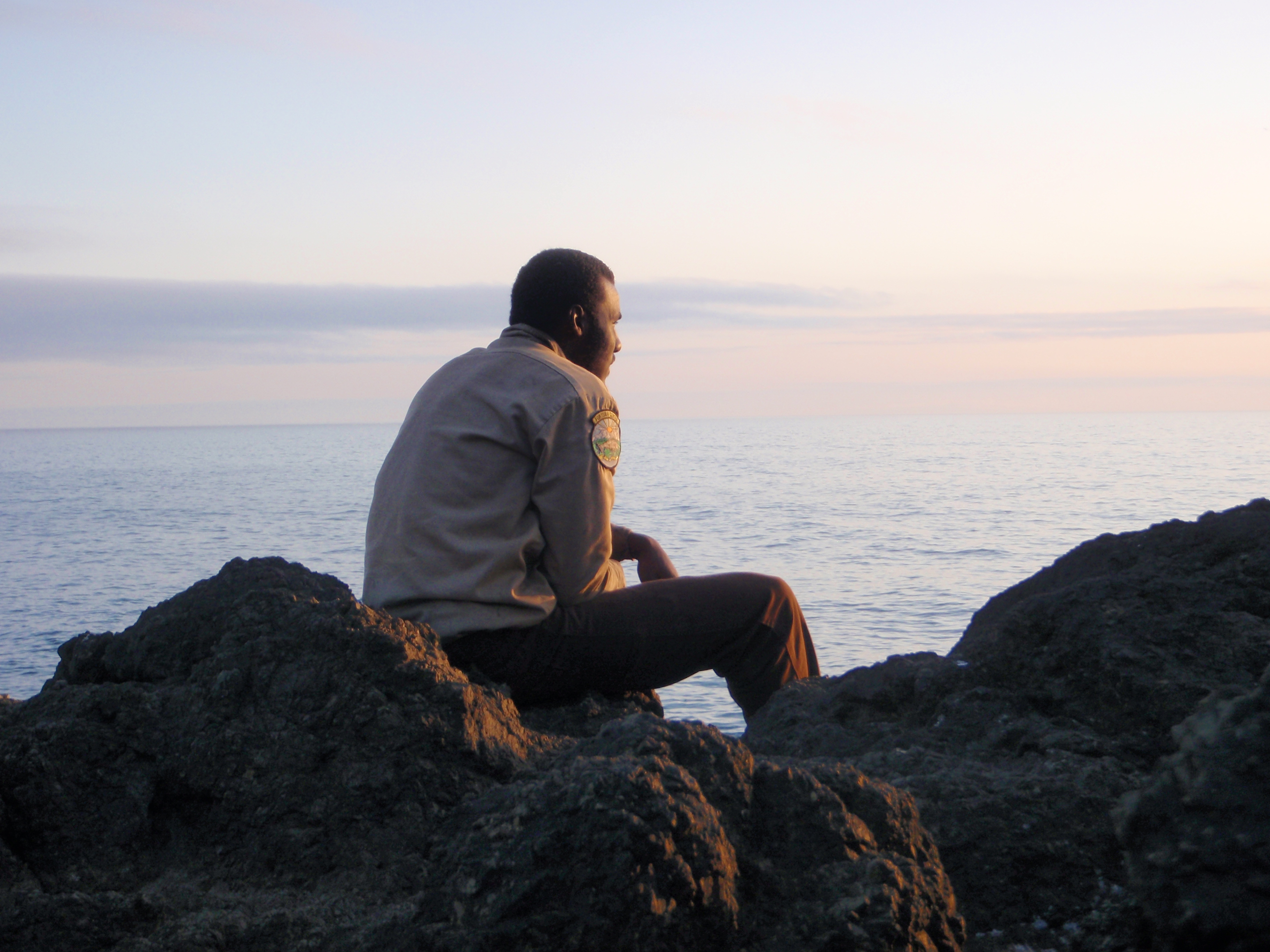 Corpsmember sitting on a rock looking at the sunset. 