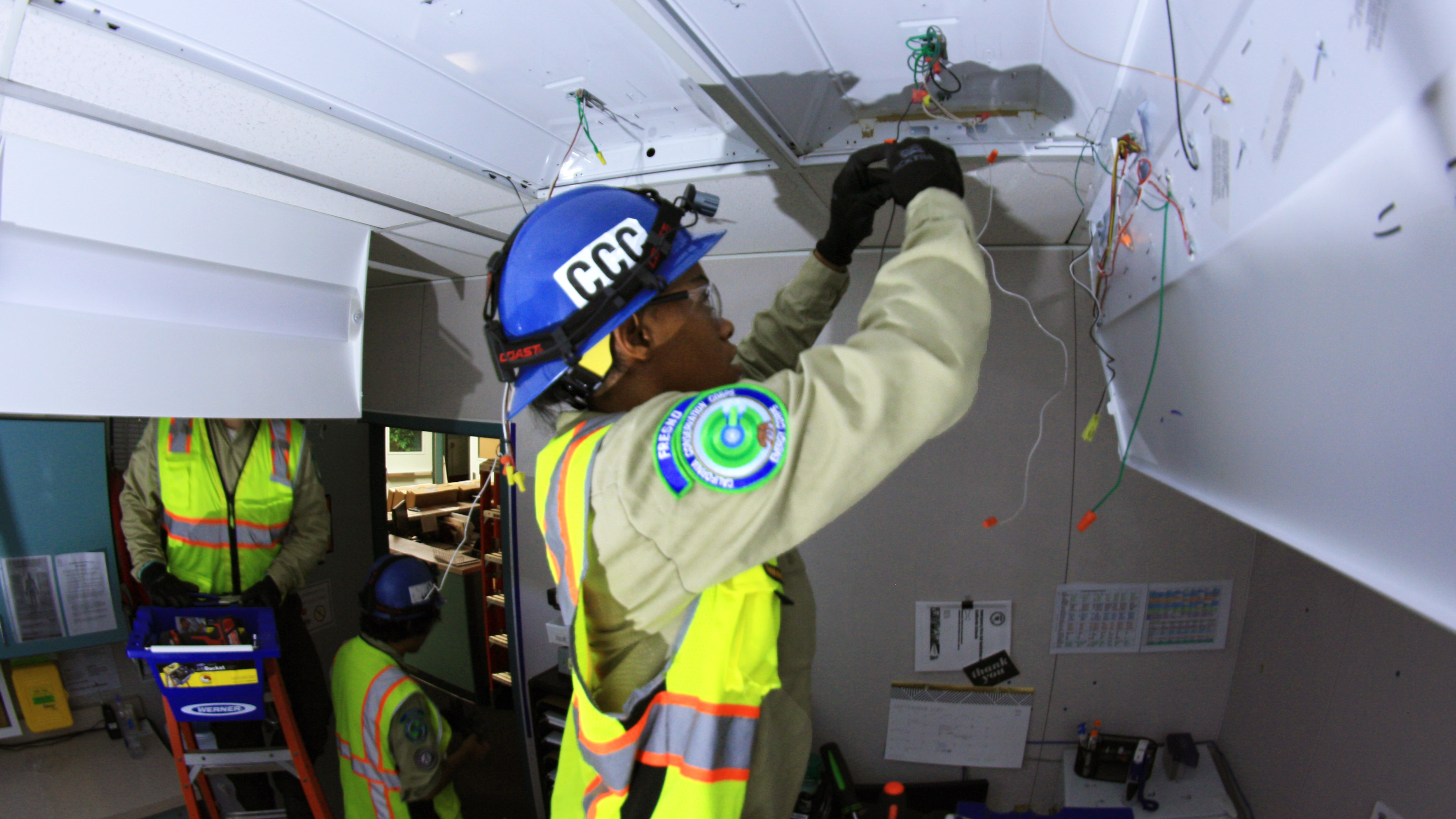 female corpsmember working on light fixture atop a ladder