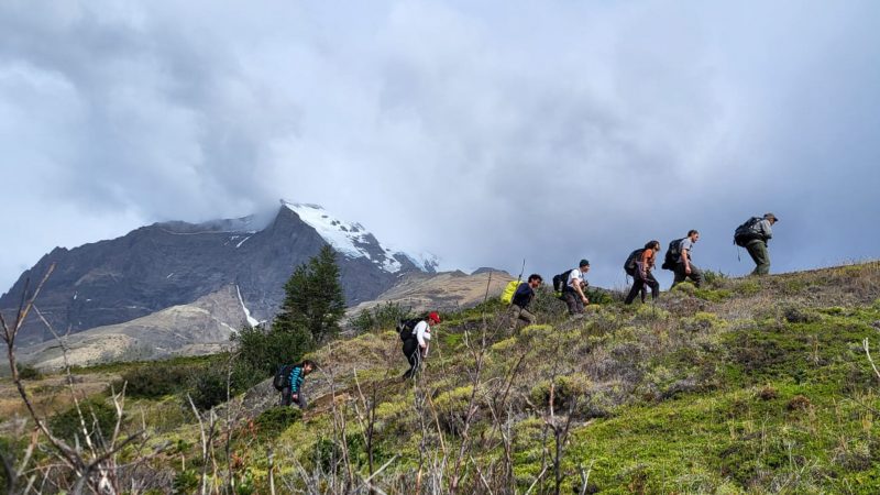 Corpsmembers hike up a slope in Patagonia with snow covered mountains in the background.