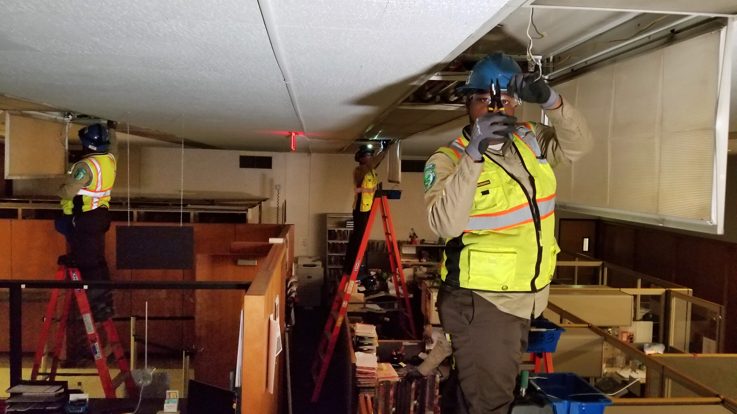 corpsmembers in vests standing atop ladders in an office building
