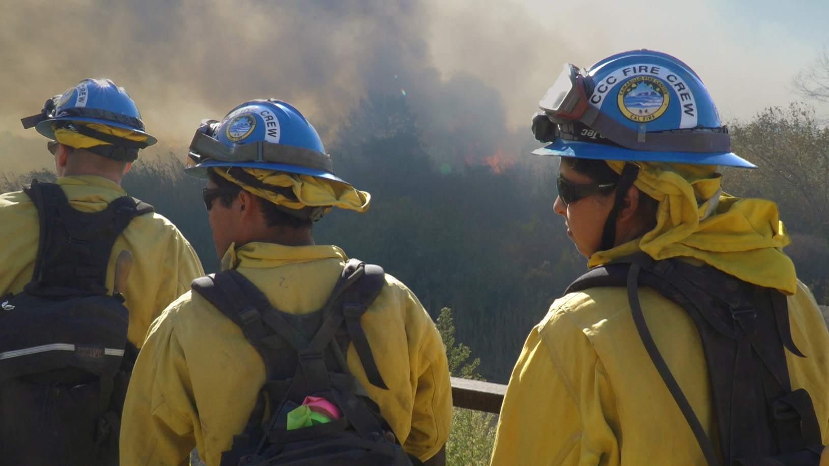 Male and female Corpsmembers listen to instructions as fire burns off in the distance