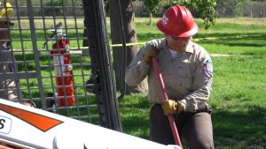 Foreground is cage of bobcat, background of photo is Corpsmember looking down at shovel blade which she's holding with two hands.