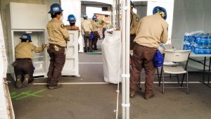 photo, corpsmembers load refrigerators with supplies inside white tents in a parking lot