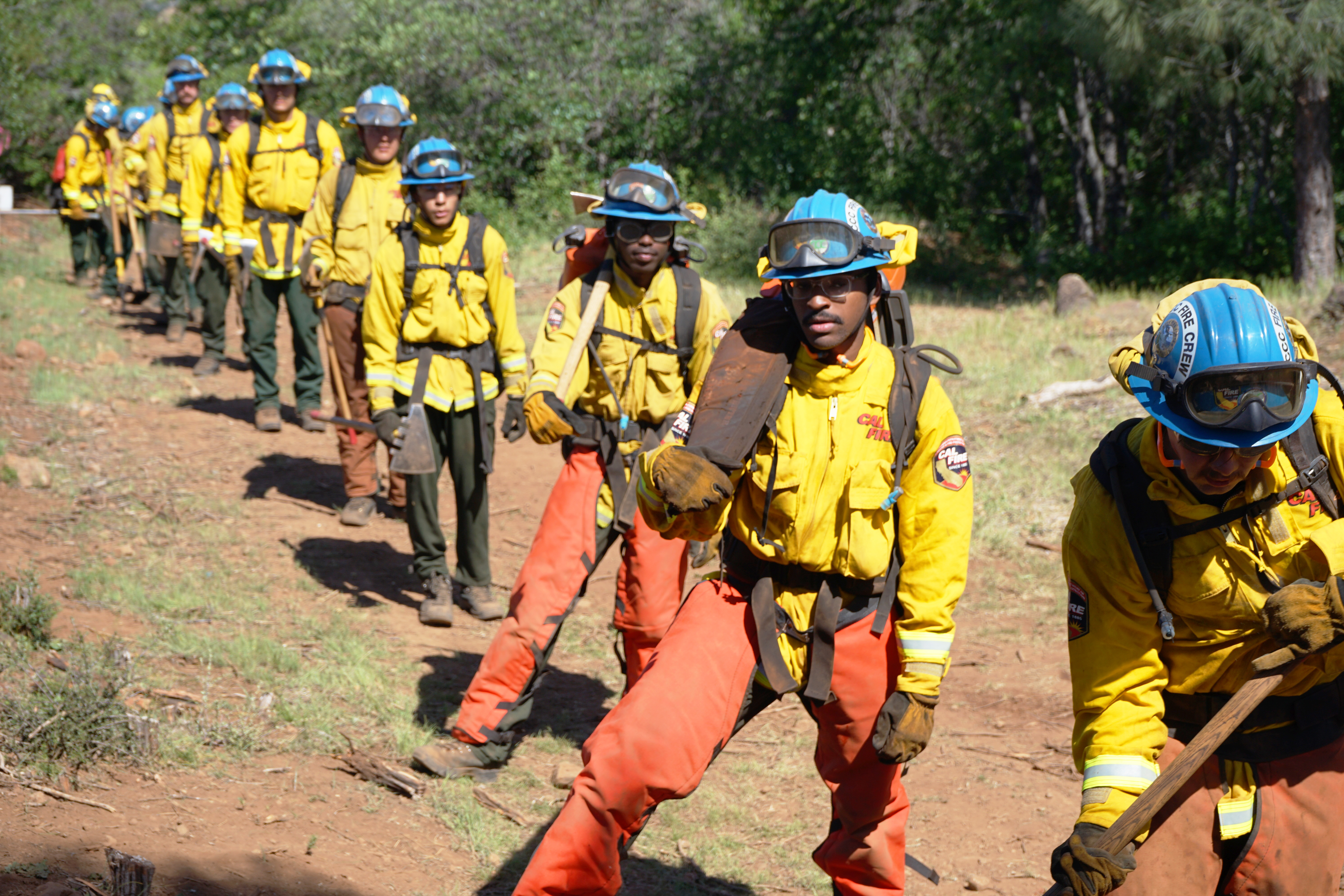 Wildland firefighters in full safety gear hold hand tools and wait for instructions