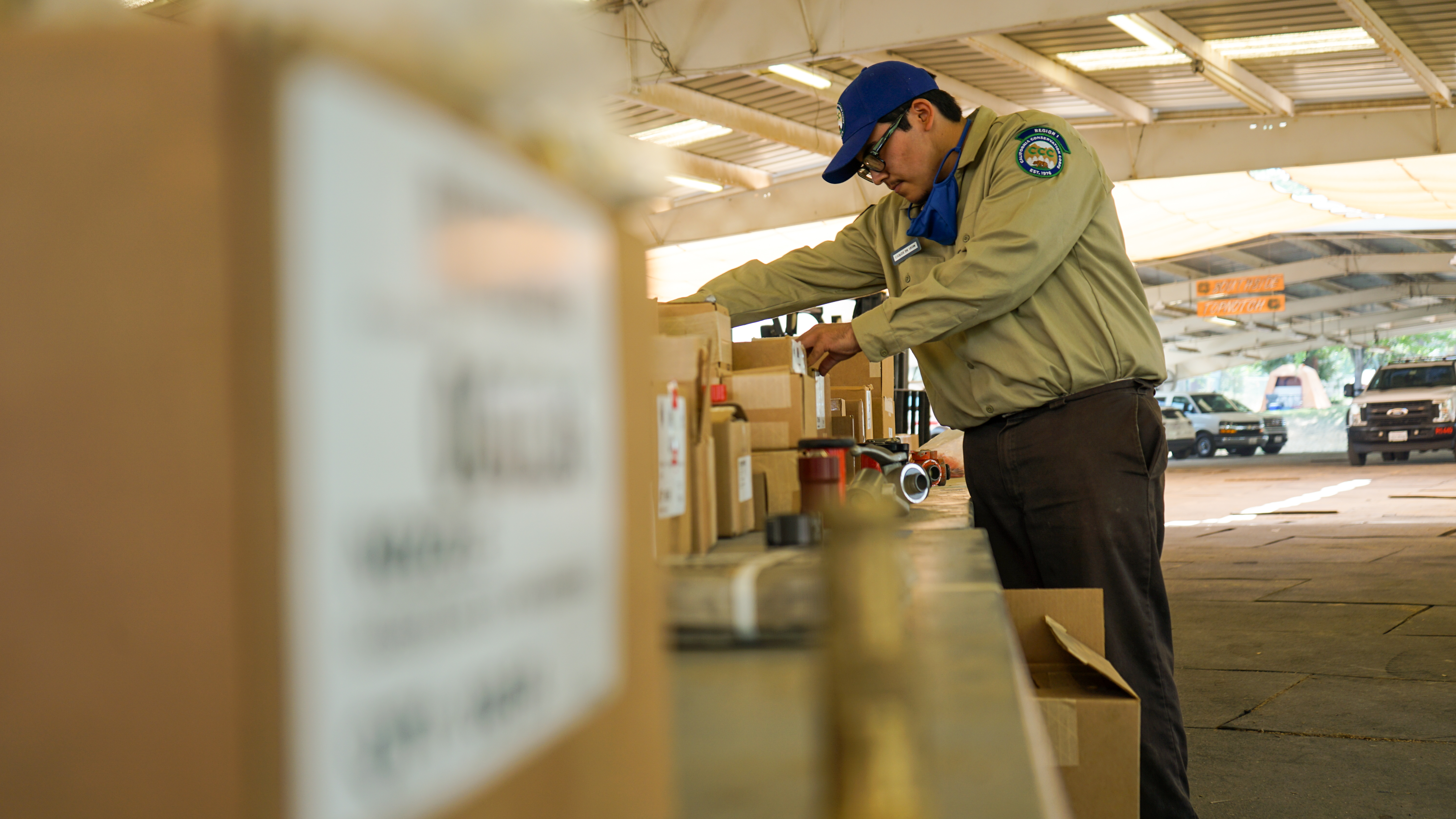 male corpsmember in background searches boxes and foreground box is out of focus