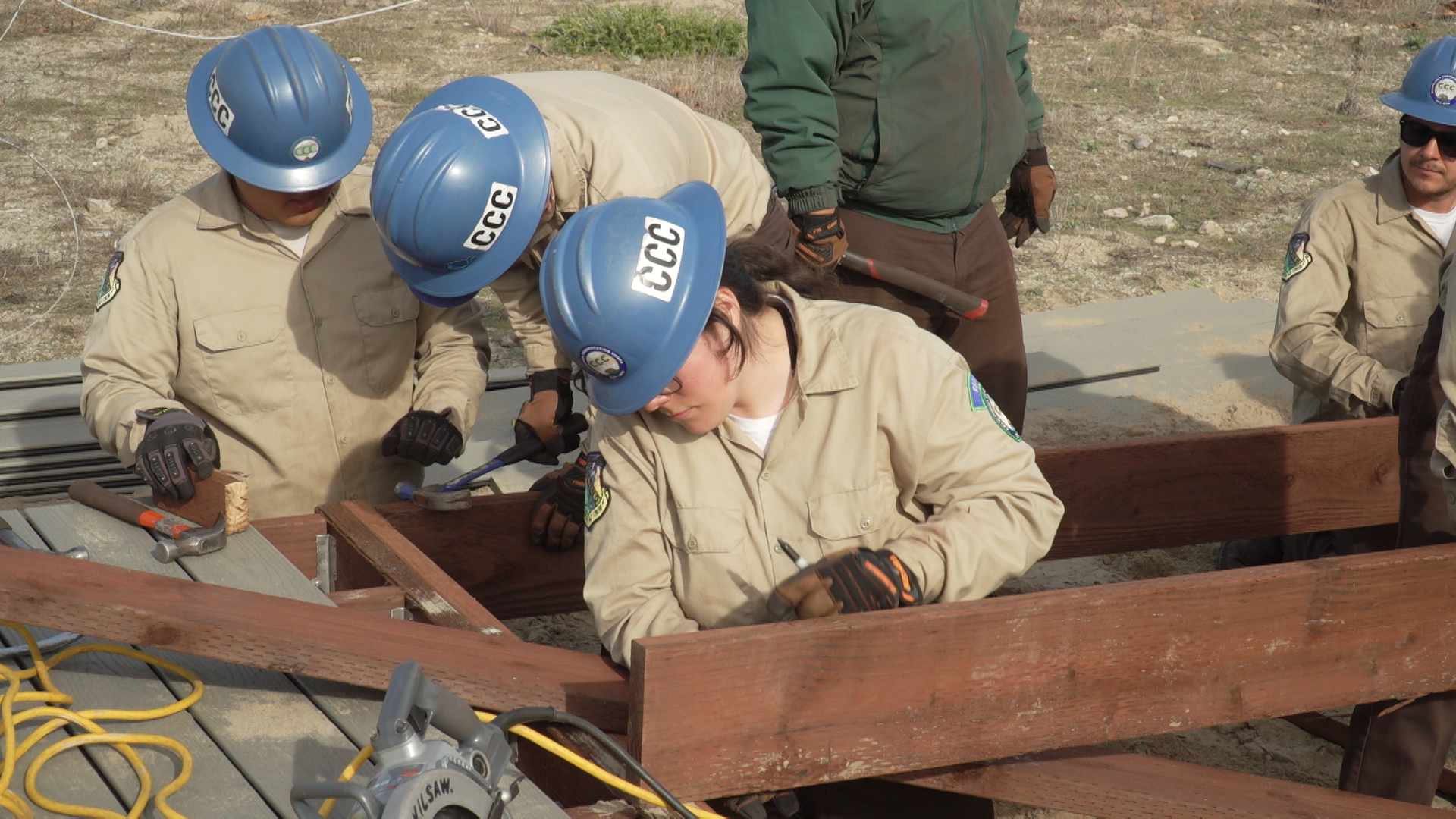 female corpsmember measures wood support beam while building boardwalk