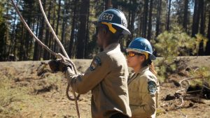 man in full ppe tying rope with female in full ppe in background