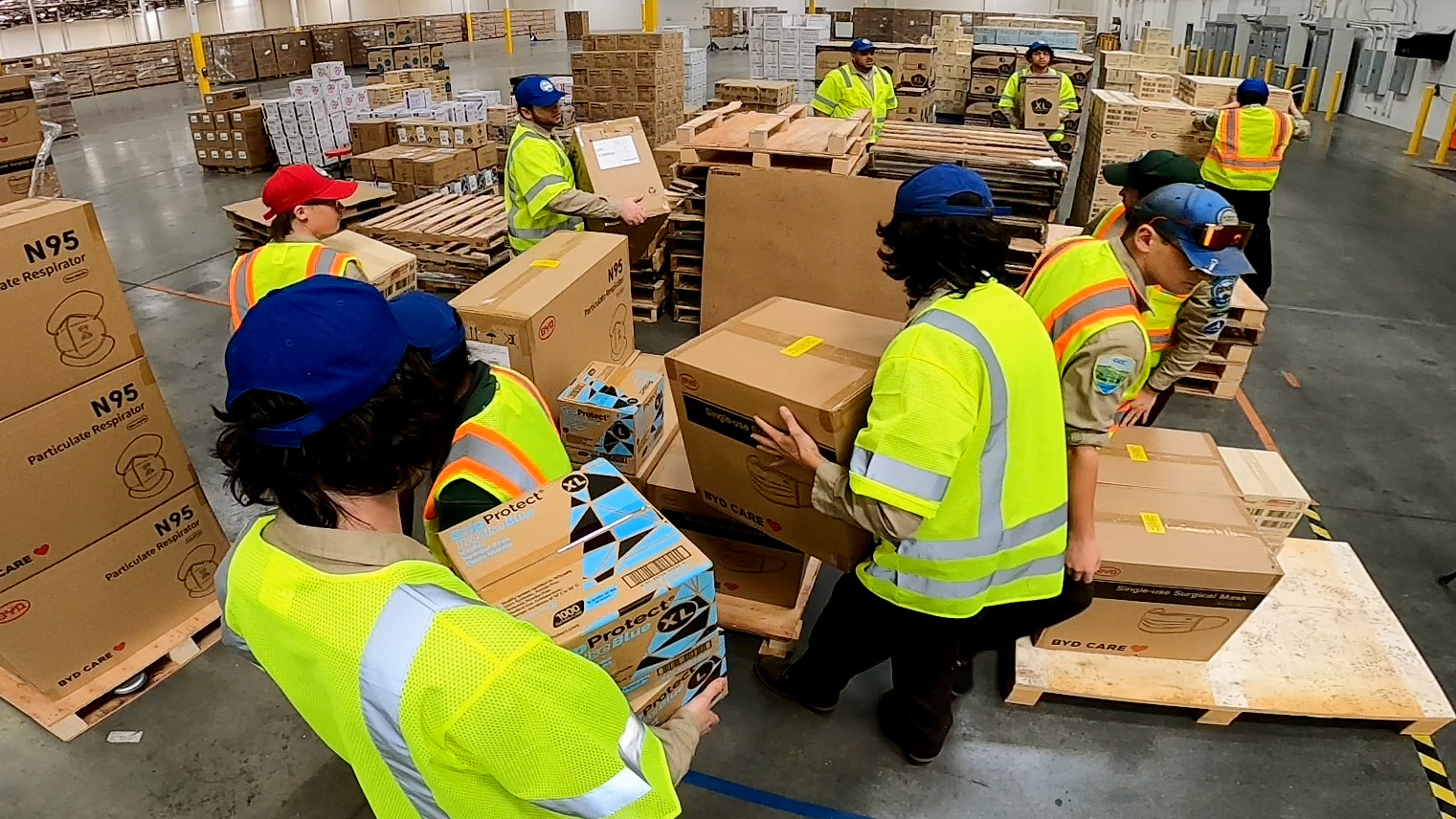 corpsmembers in safety vests moving boxes in warehouse