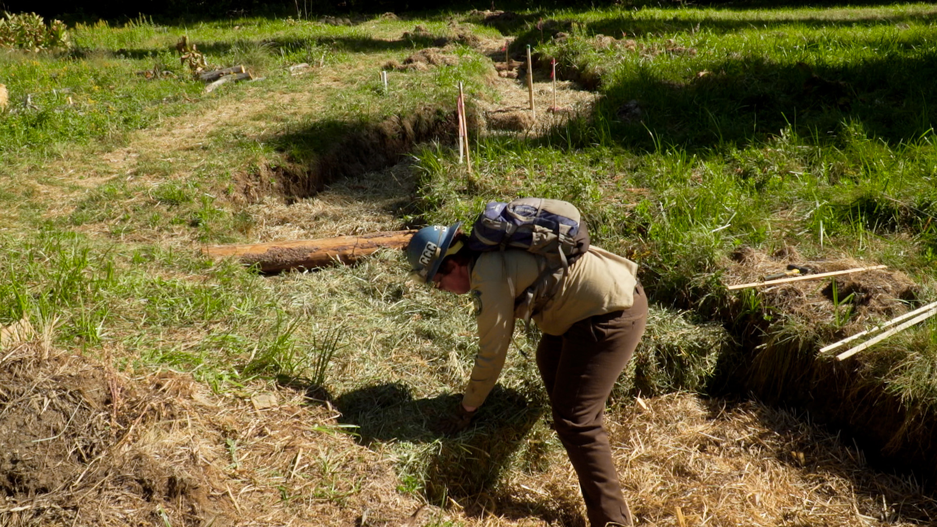 a corpsmember places a hay bale in a damaged meadow