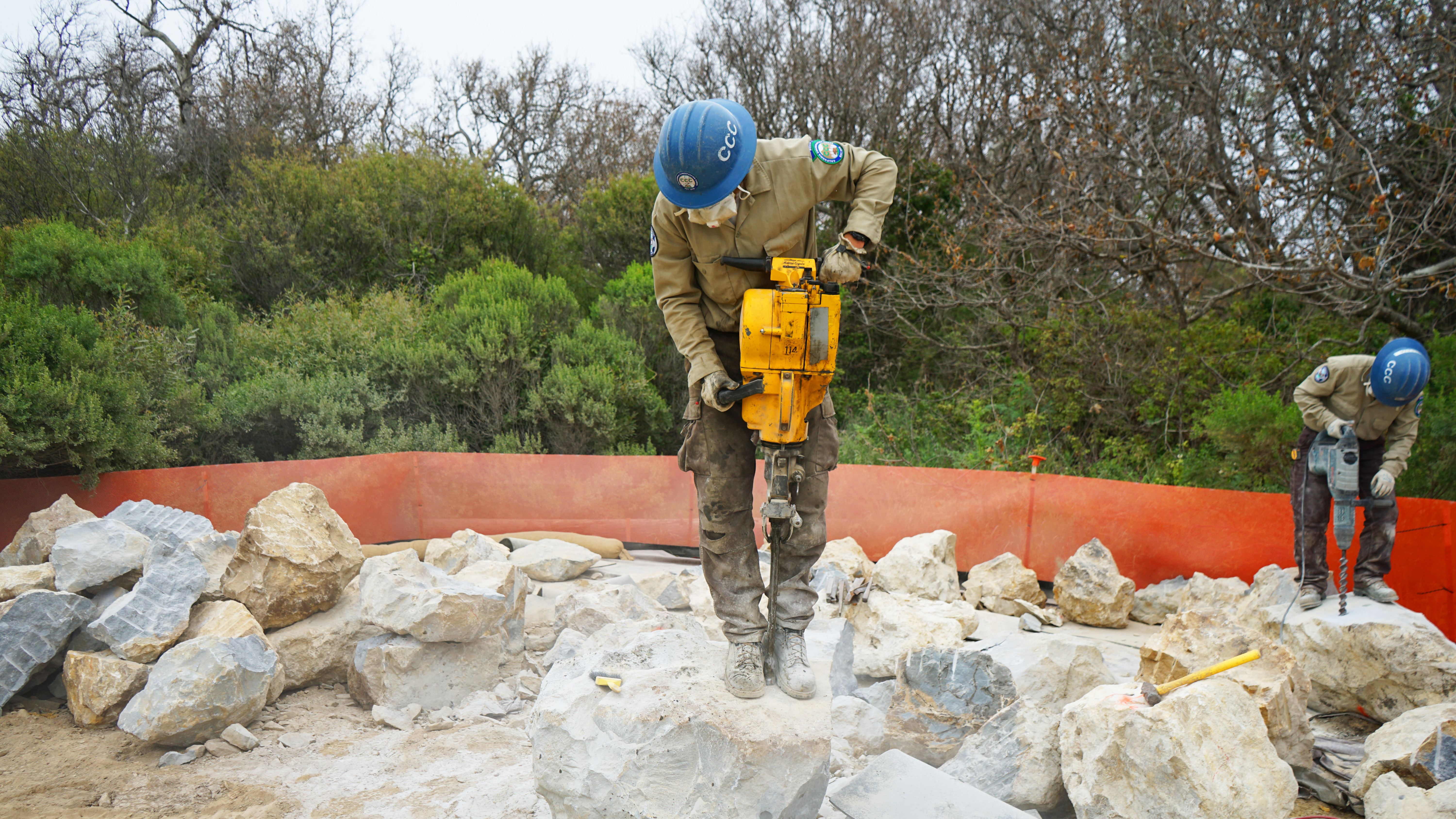 Two Corpsmembers drill holes into rock. 