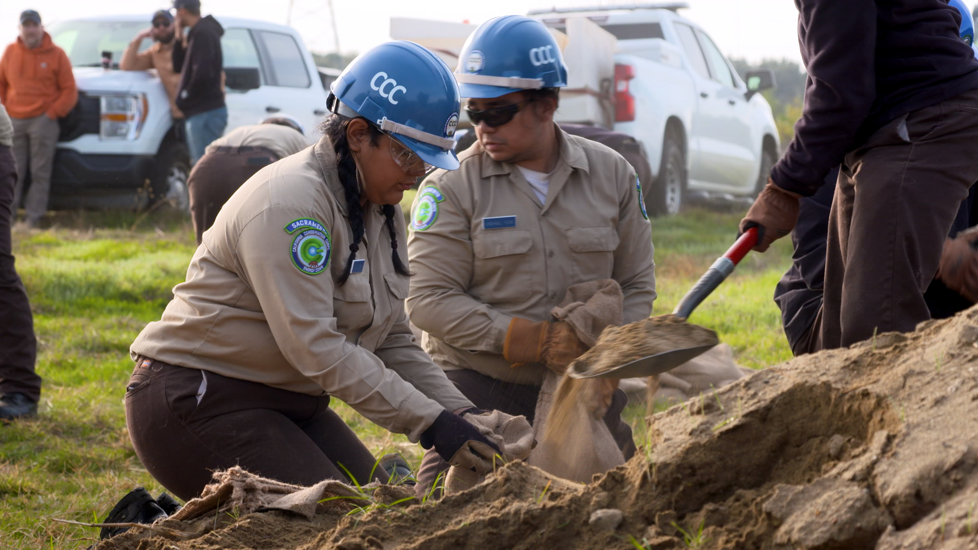 female corpsmember on knees holding sand bag open for shovel