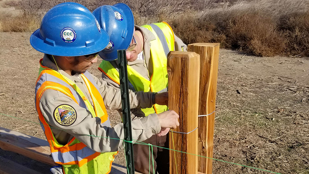 Corpsmembers wrapping wire around a fence post