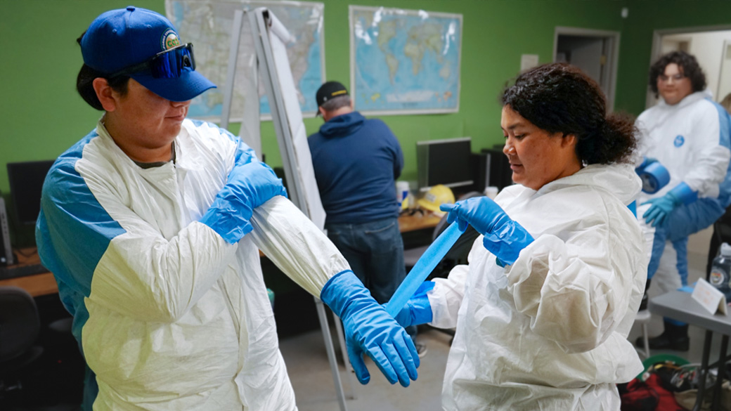 corpsmember taping up another corpsmember's ppe
