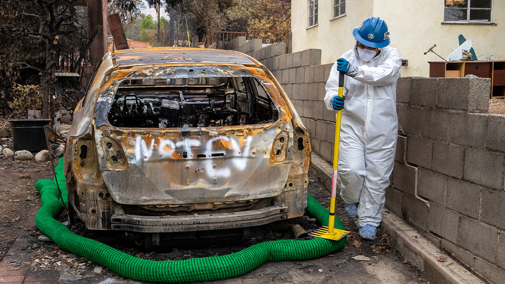 corpsmember in tyvek walking around burned car using mcleod on a silt sock