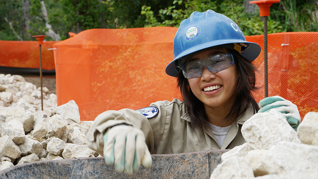 corpsmember smiles while putting rocks in a wheelbarrow