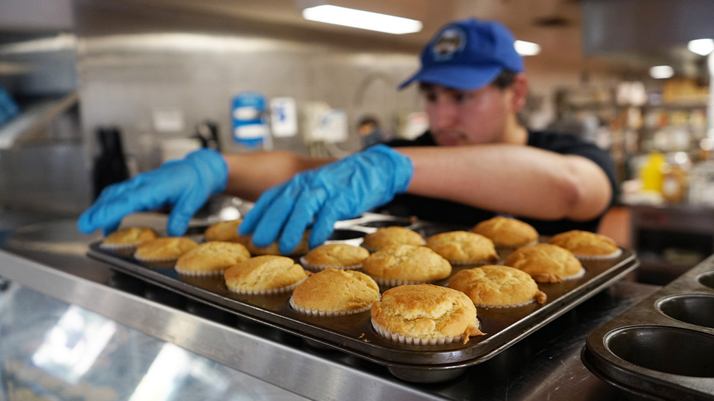 corpsmember wearing gloves pulls muffins from a tray