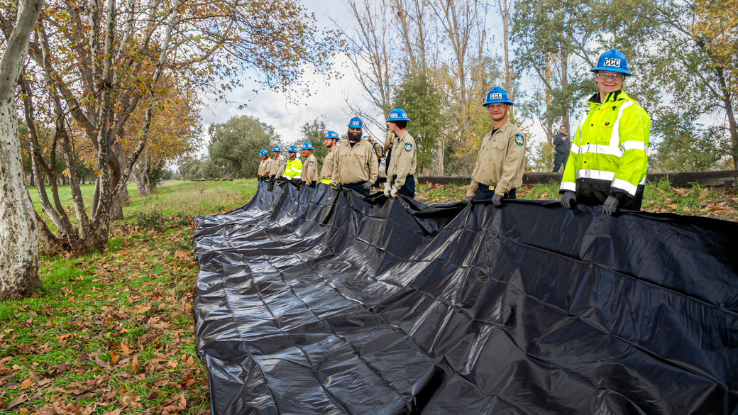 Corpsmembers hold up a large sheet of plastic visqueen.