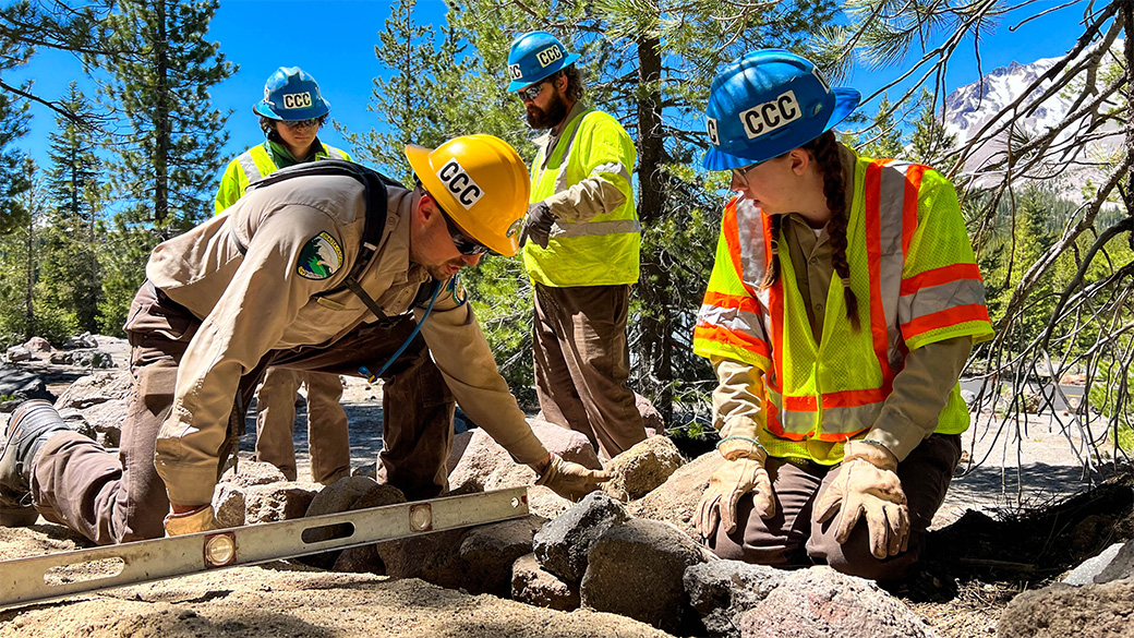 Corpsmember and staffer on hands and knees on a trail