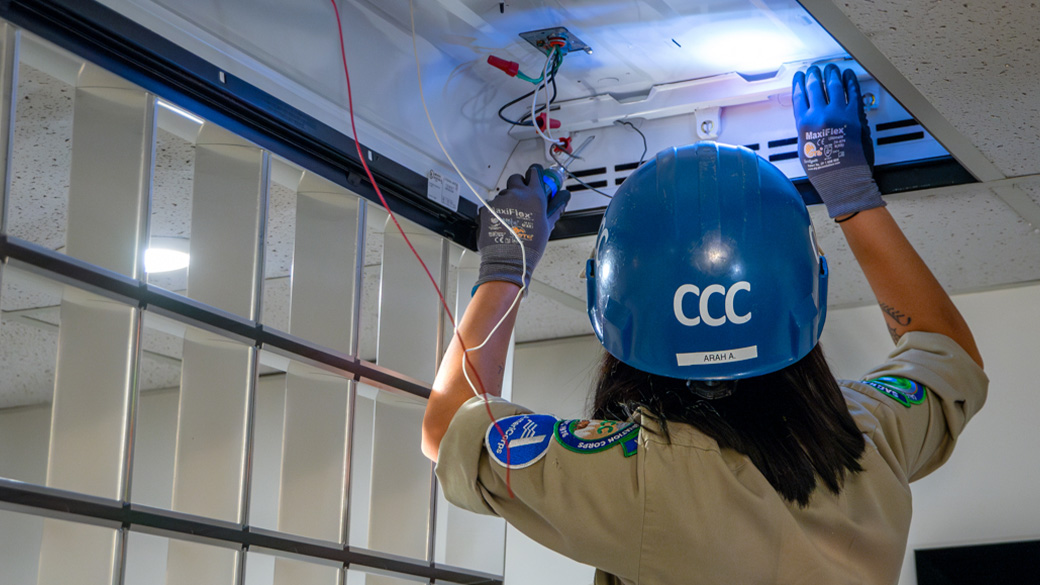 corpsmember looking into open light fixture with headlamp on