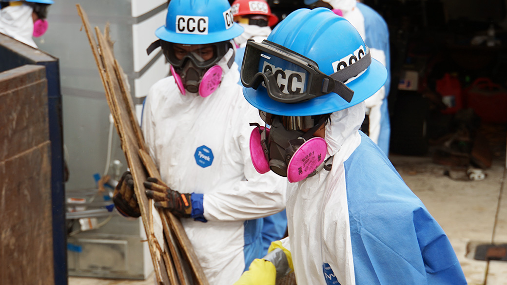 corpsmembers in respirators and protective equipment hauling debris