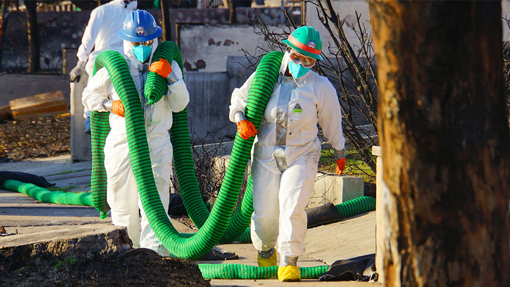Corpsmembers in tyvek carrying silt sock on their shoulders.