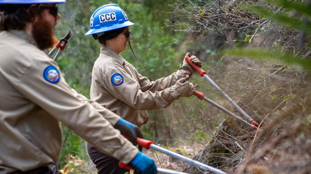 corpsmembers in uniform using loppers to cut vegetation