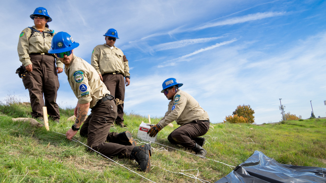 corpsmembers kneeling on hillside tying ropes to stakes