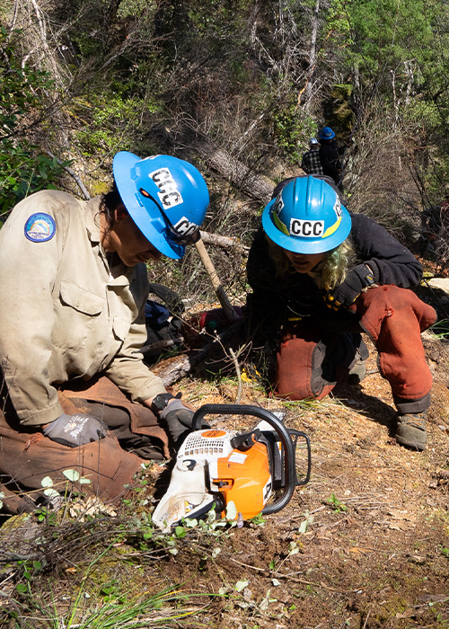 SideImage_Siskiyou_500x700 Corpsmembers on the ground cleaning their chainsaw.