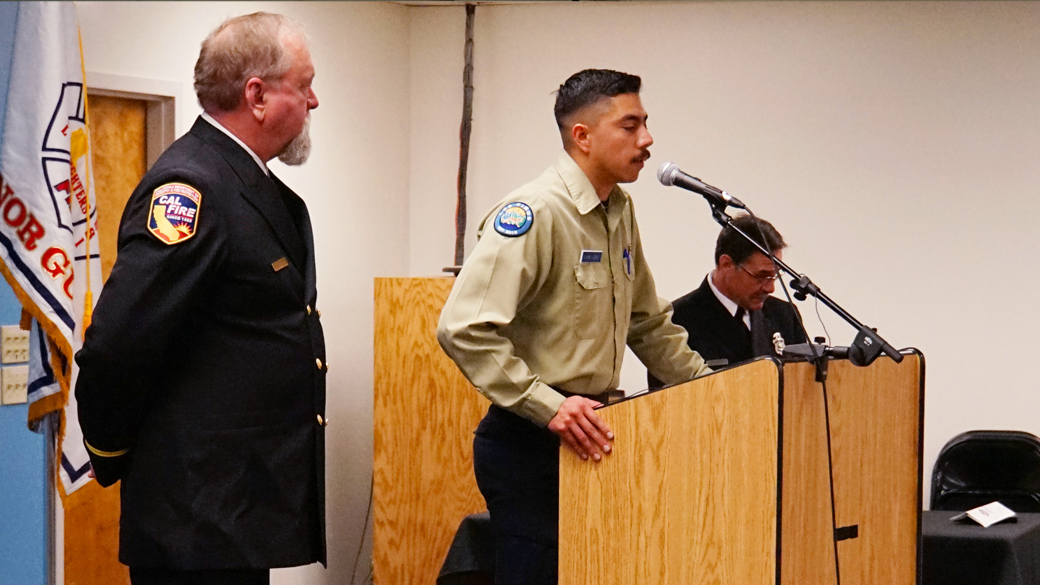 corpsmember speaking at podium while a cal fire captain watches nearby