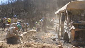 corpsmembers hitting hammers in dusty area with bus nearby