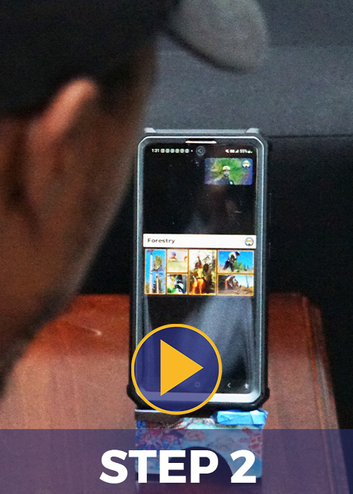 Photo of a person watching a Zoom meeting on their phone. Image has text saying Step 2 with a play button.