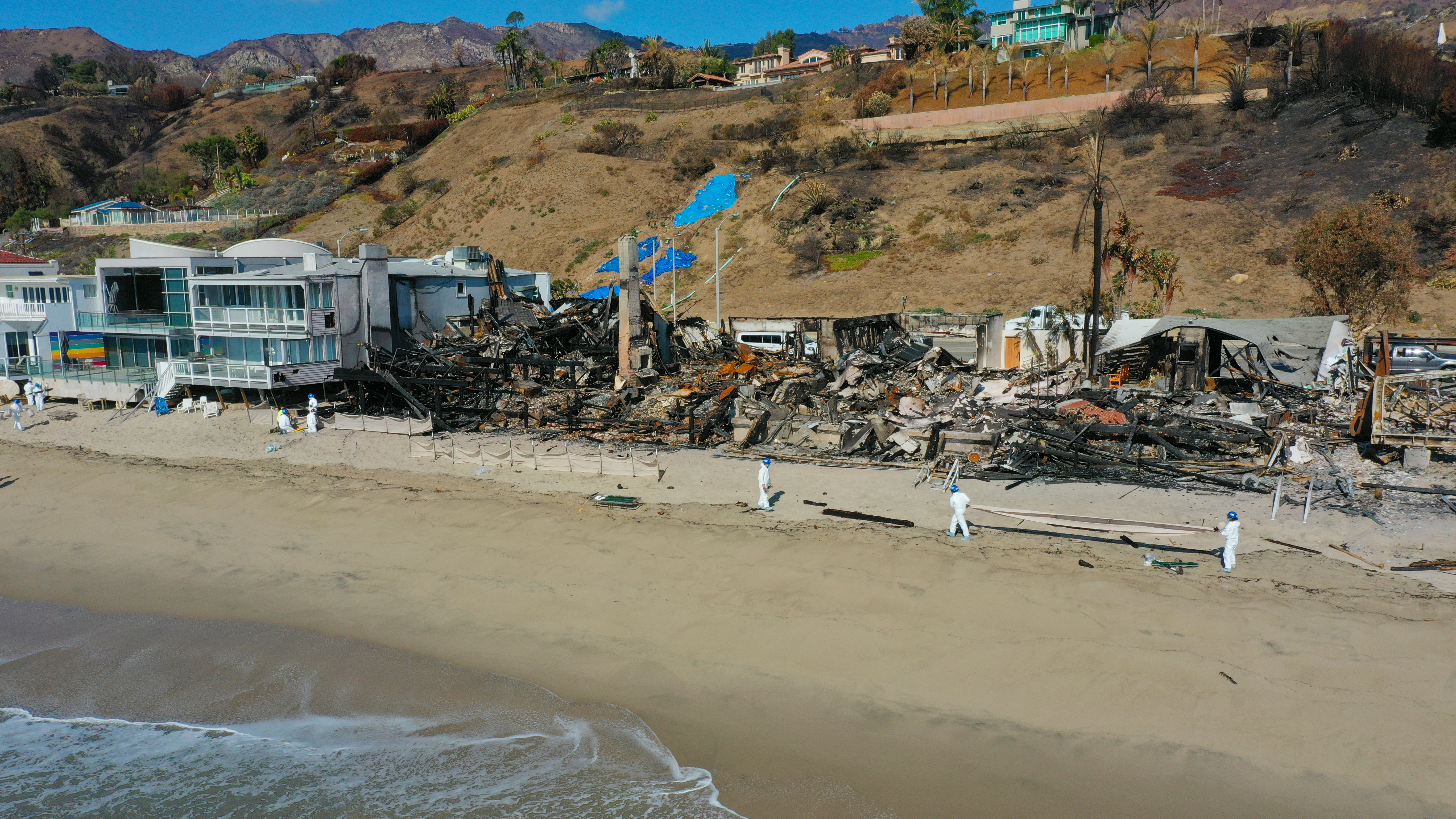 aerial photo of corpsmembers working on a beach in front of burned structures