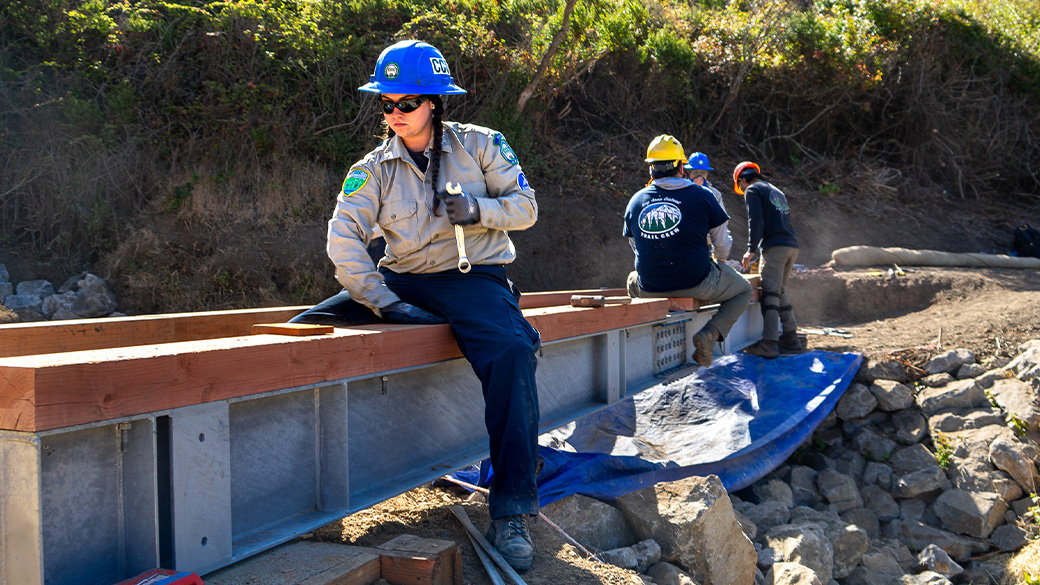 female sitting on girder installing wood with others in the background