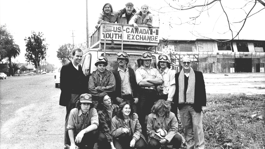Black and white image of youth posting behind a van that reads US-Canada Youth Exchange.