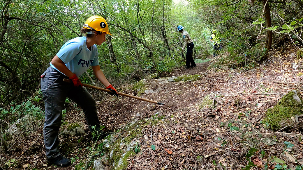 female using hand tool to clear leaves on a trail
