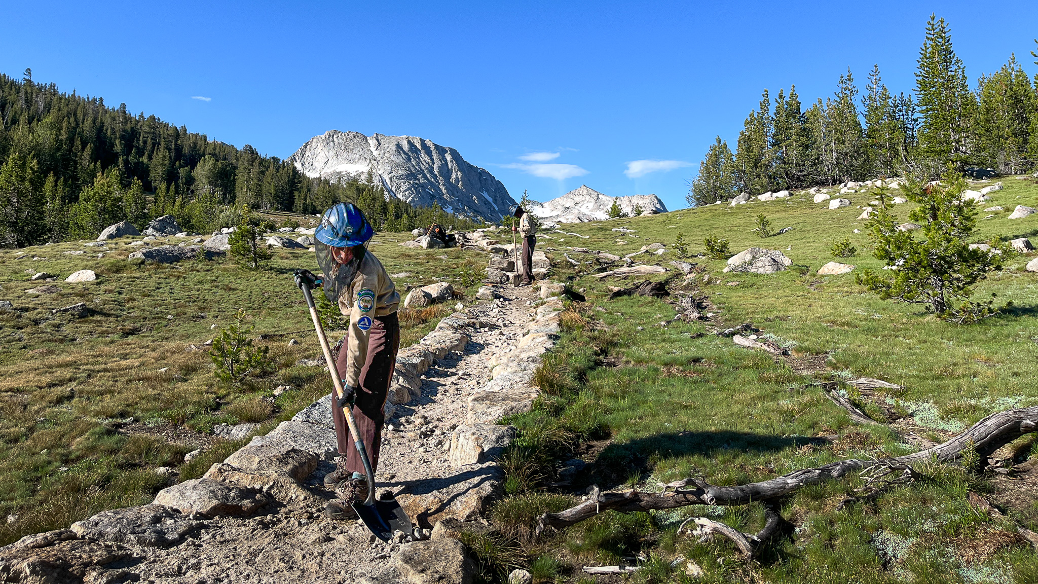 CCC Corpsmembers wear bug nets over their heads and use shovels to maintain a backcountry trail.