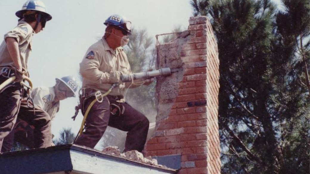 Corpsmember taking apart chimney, after earthquake cleanup.