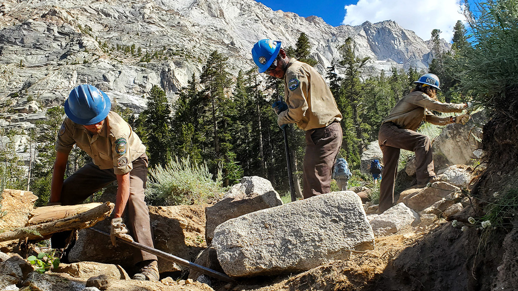 An Inyo Backcountry Trail Crew uses rock bars and other hand tools to build new trail out of rock.