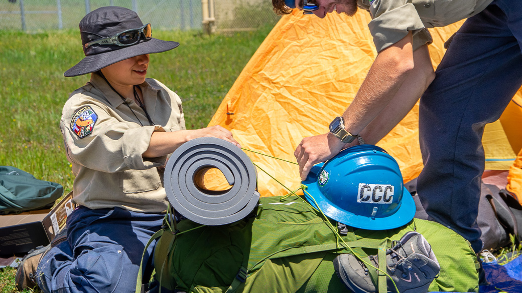 corpsmember rolling up gear onto backpack