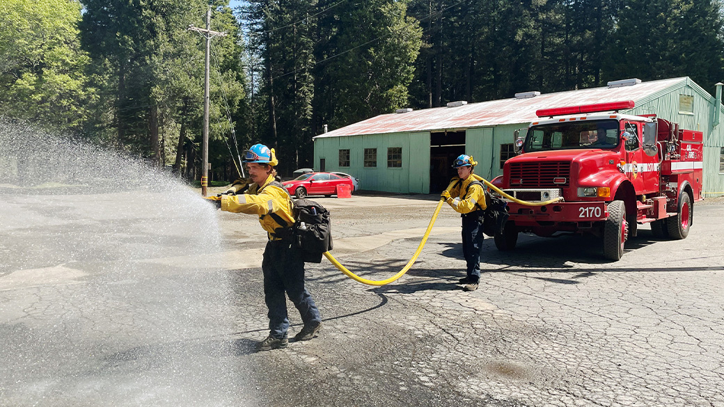 corpsmembers use fire hose near a fire truck in a parking lot