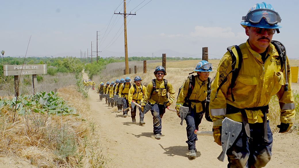 corpsmembers in fire gear hiking up a dusty road