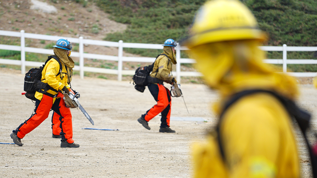 corpsmembers in background holding chain saws in full fire gear