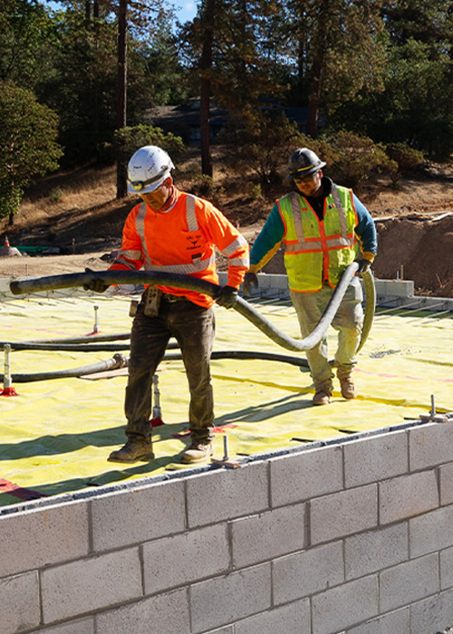 two construction workers holding cement pump hose