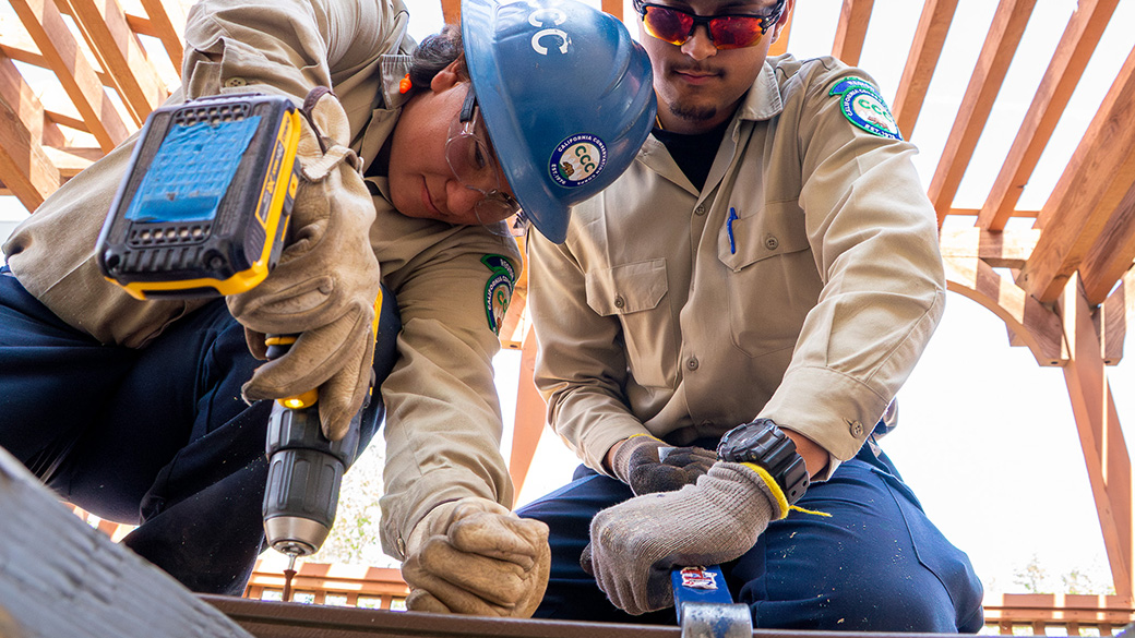 Inland_Resource_ScrewInstall_032725_1040x585 female corpsmember uses drill to insert screw while male corpsmember uses pry bar to hold deck board in place