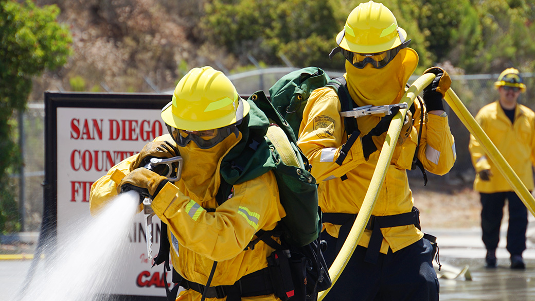 firefighters in full gear haul hose during training