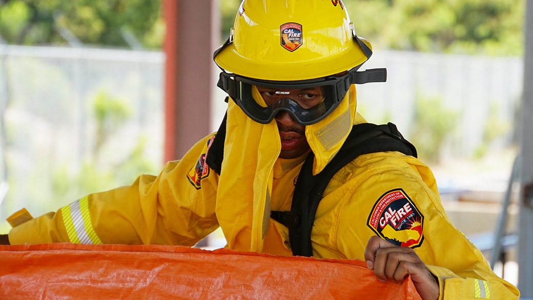 male in full wildland fire gear holding a plastic tarp practice shelter