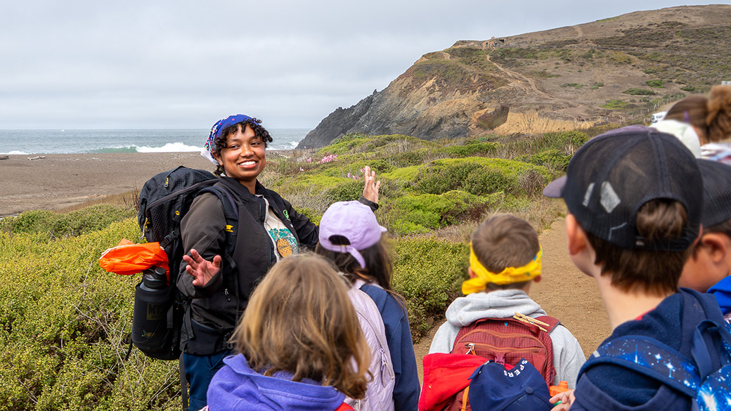 Female leading hike near beach with young campers blurred out in foreground